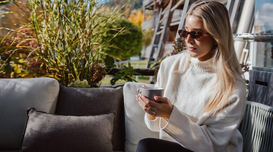 Dame trinkt Kaffee in der Sonne auf einer Gartencouch