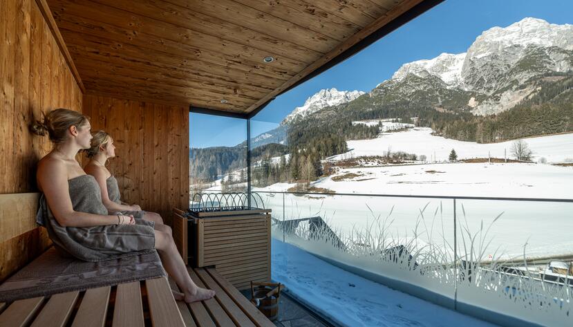 Two women in the sauna with a view of the snow.