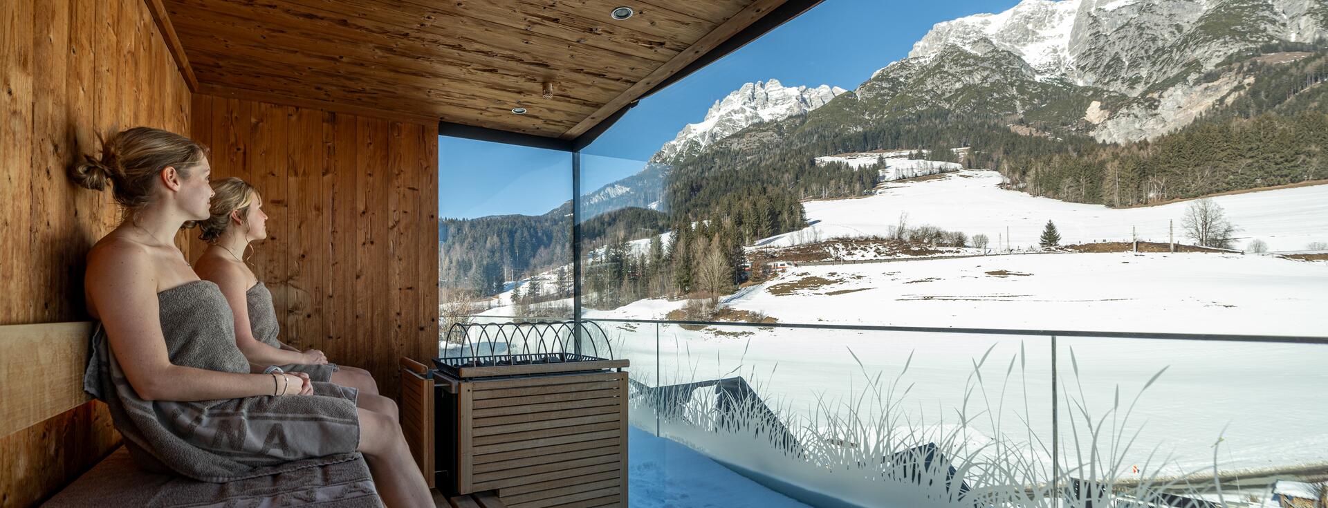 Two women in the sauna with a view of the snow.