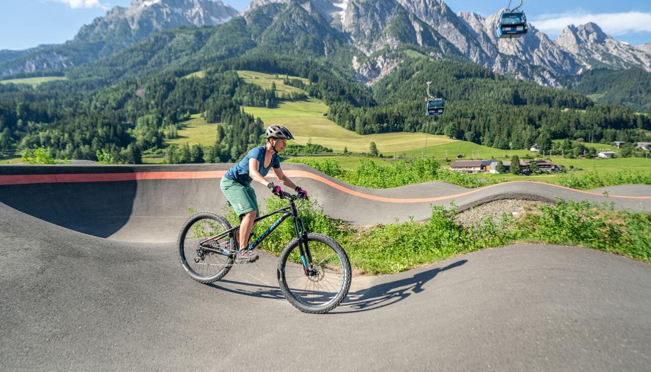 Frau fährt mit Mountainbike auf Pumptrack vor Bergkulisse