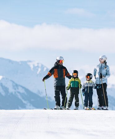 Familie steht auf Skipiste mit Bergkulisse im Hintergrund