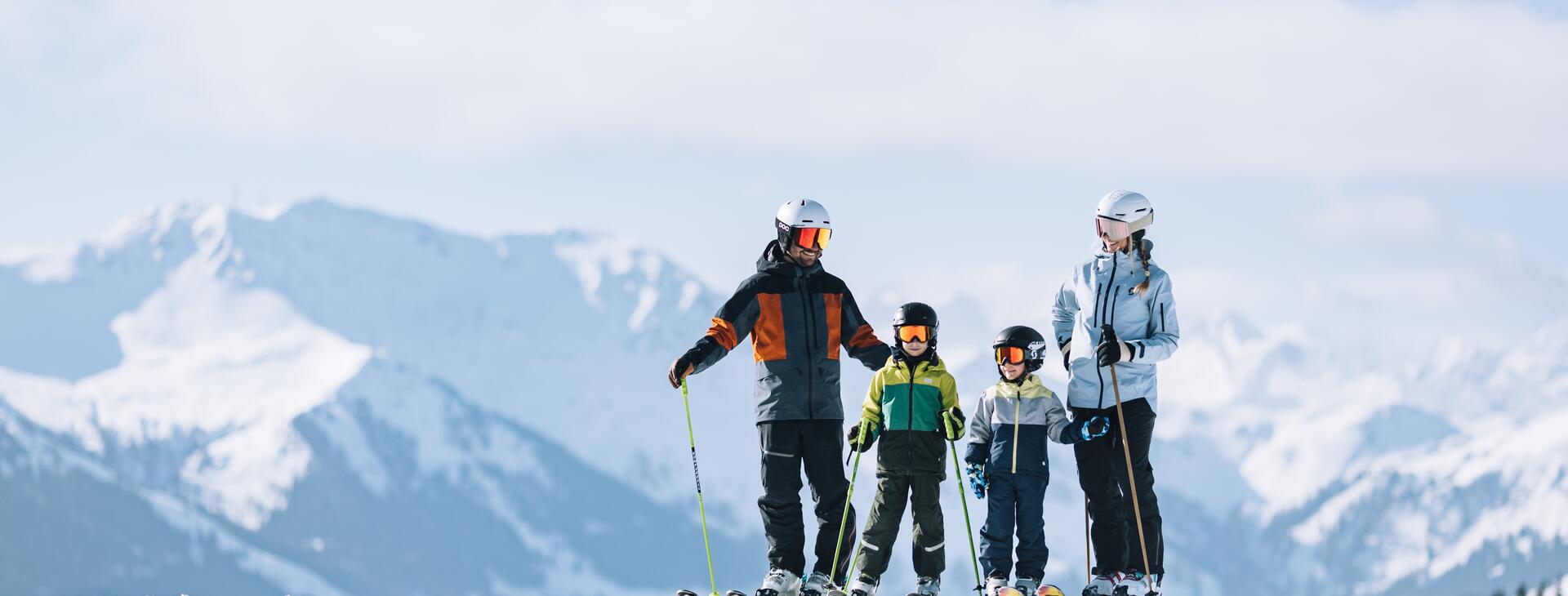 Familie steht auf Skipiste mit Bergkulisse im Hintergrund