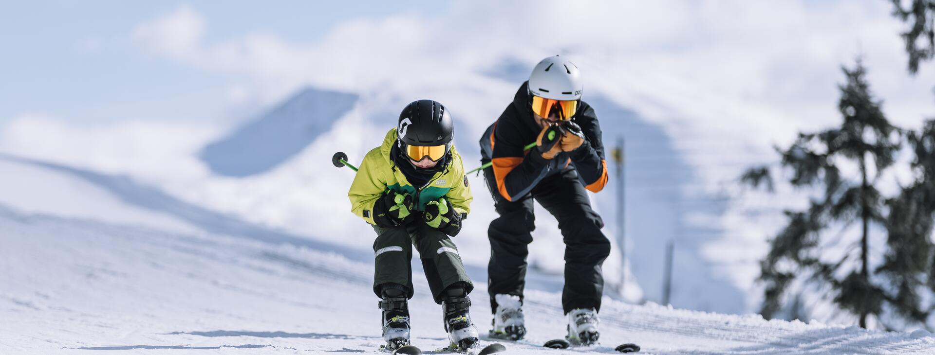 Father and son ride down the ski slope in a crouching position.