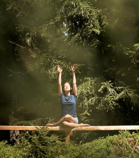 Frau sitzt in Yogapose auf Holzbalken im Wald